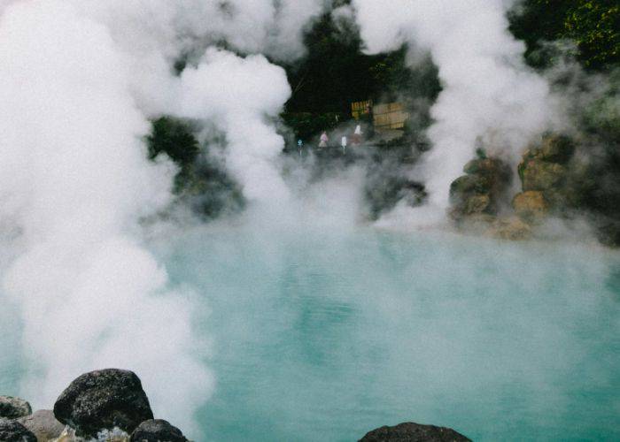 A close-up of an onsen hot spring in Japan; steam is rising from the blue waters.